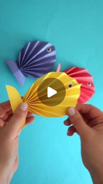 two paper fish are being held up by someone's hands on a blue background