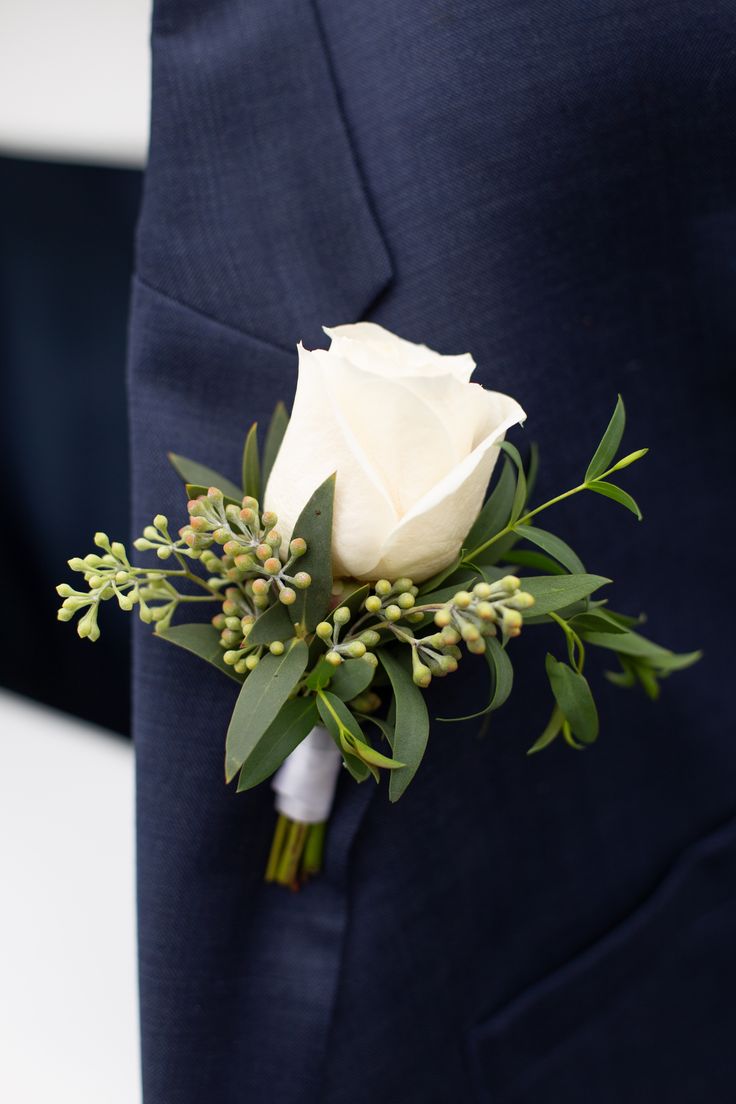 a boutonniere with white flowers and greenery on it's lapel