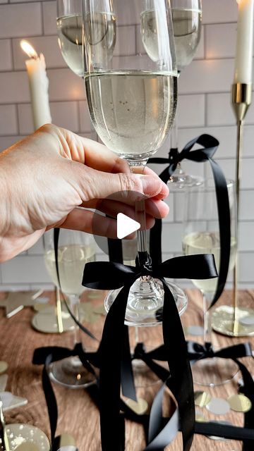 a person holding a wine glass in front of some glasses on a table with candles and confetti