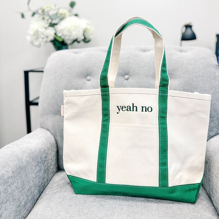 a white and green tote bag sitting on top of a gray couch next to a vase with flowers