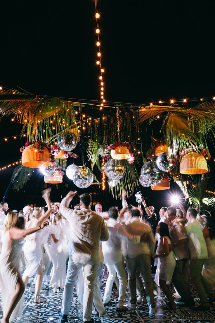 a group of people dancing in front of hanging lights and disco ball decorations at night