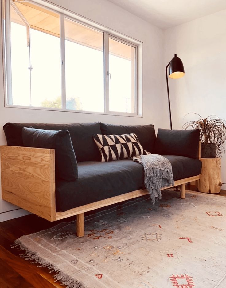 a black couch sitting on top of a wooden floor next to a rug and window