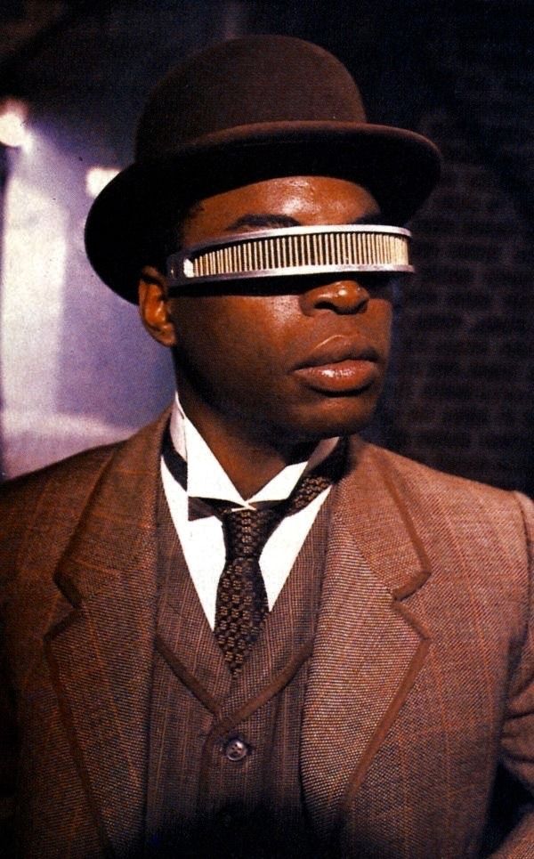 a man in a suit and tie with a blindfold on his face wearing a hat