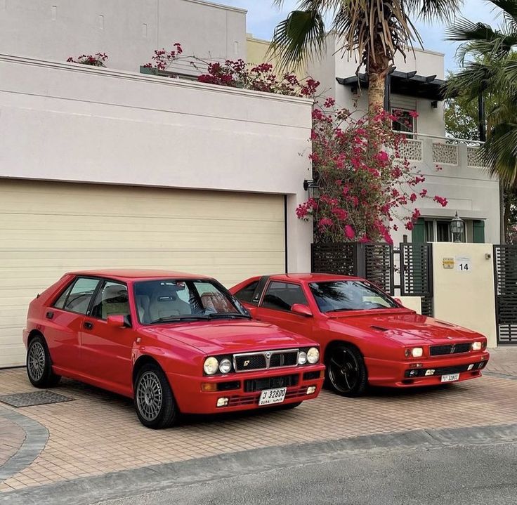 two red cars parked next to each other in front of a building with palm trees