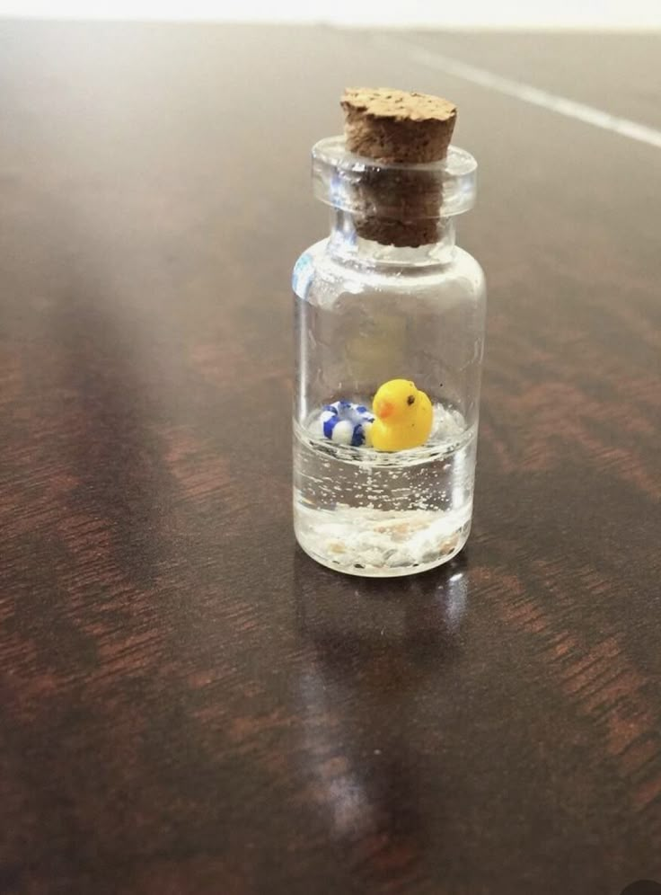 a small yellow rubber duck in a glass bottle on a wooden table with a cork top