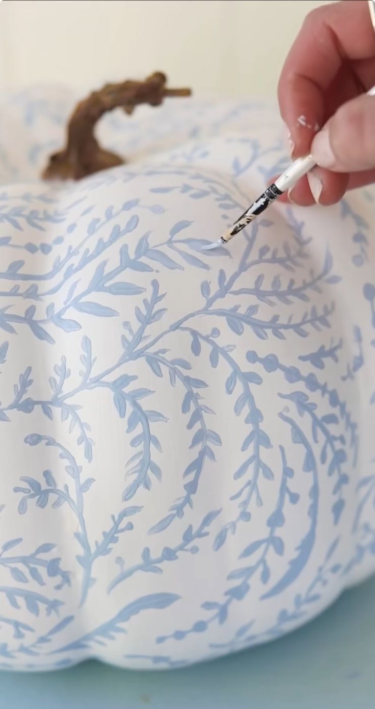 someone is painting the inside of a decorative pumpkin with blue and white designs on it