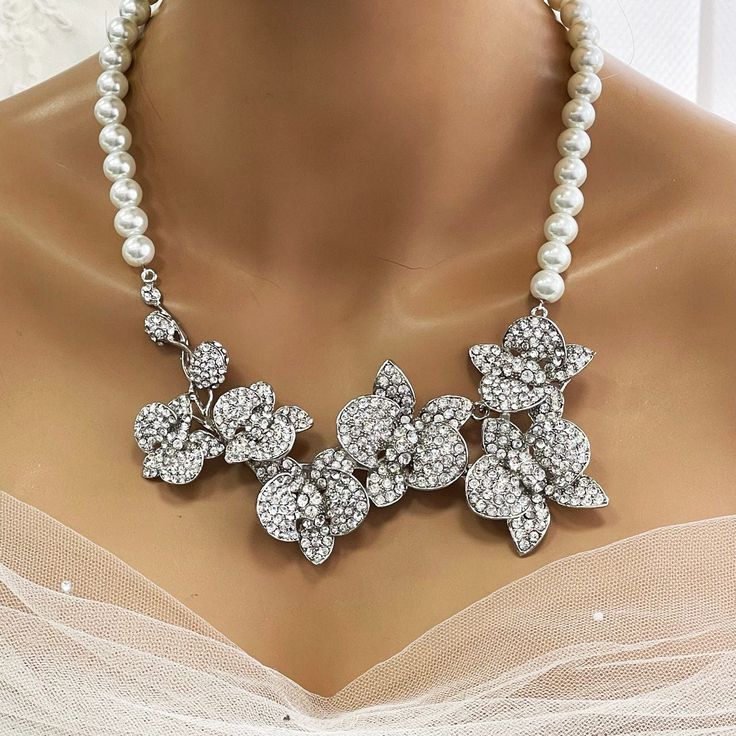 Elevate your bridal look with our Bridal Statement Earrings Necklace Set. Crafted with stunning crystal pearls and intricate orchid flowers, this unique wedding jewelry set adds a touch of elegance to your special day. Designed as the perfect gift for brides, each piece reflects meticulous attention to detail and timeless beauty. Let our set be a cherished part of your unforgettable moments. Embrace authenticity and sparkle with this exquisite ensemble. Dazzle on your special day with our exquis White Crystal Embellished Bridal Earrings For Wedding, White Flower Bridal Necklace For Wedding, White Floral Bridal Necklace For Wedding, White Pearl Bridal Necklace With Rhinestones, White Crystal Embellished Bridal Necklace, White Crystal Embellished Bridal Necklace For Wedding, Silver Flower Bridal Necklace For Wedding, Silver Pearl Necklace With Rhinestones For Wedding, Pearl White Crystal Bridal Earrings For Wedding