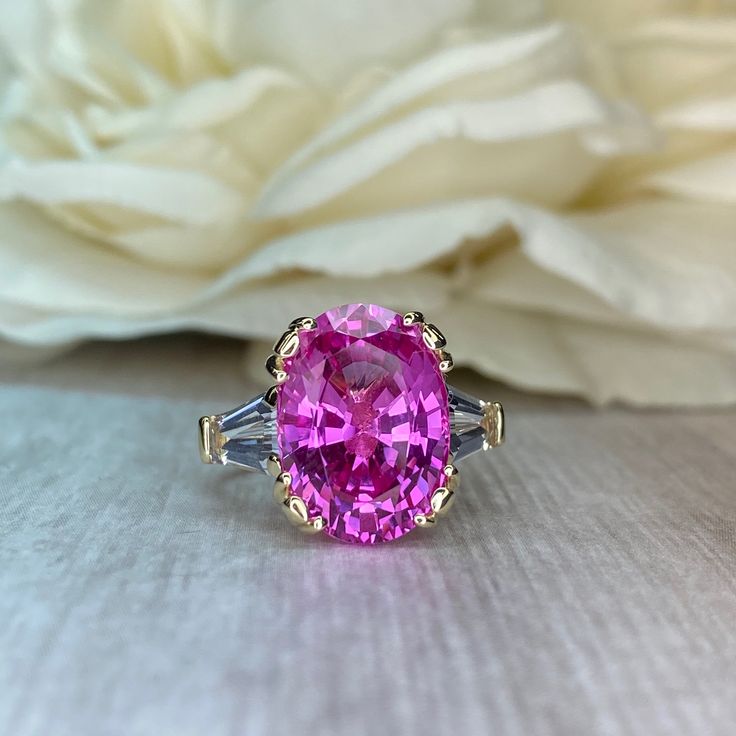 a pink ring sitting on top of a table next to a white flower and cloth