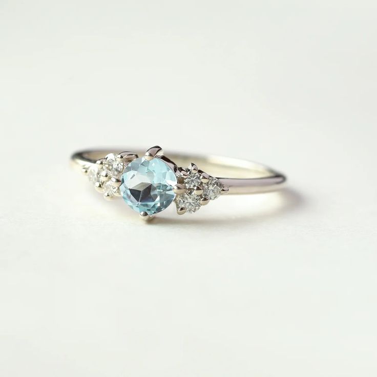 Dainty, yet powerful the Irene ring with round Swiss Blue Topaz is one of those rings you put on and it instantly lifts you up and makes you feel good. There is something in the Swiss Blue Topaz, the stone of abundance and feminine energy that makes this ring stand out and look beautiful on any lady. Together with side Moissanites, this is the perfect ring to treat yourself to. Details: Center stone Gemstone: Swiss Blue Topaz Stone Shape: Round Measurements: 5mm Side stones Gemstone: Moissanite Sapphire Topaz Round Ring For Promise, Sapphire Topaz Promise Ring, Sapphire Topaz Ring For Promise, Blue Topaz Cluster Ring For Anniversary, Promise Blue Topaz Diamond Ring In Round Cut, Round Aquamarine Diamond Ring With Gemstone, Promise Blue Topaz Diamond Ring With Round Cut, Aquamarine Diamond Promise Ring, Blue Topaz Cluster Ring For Promise