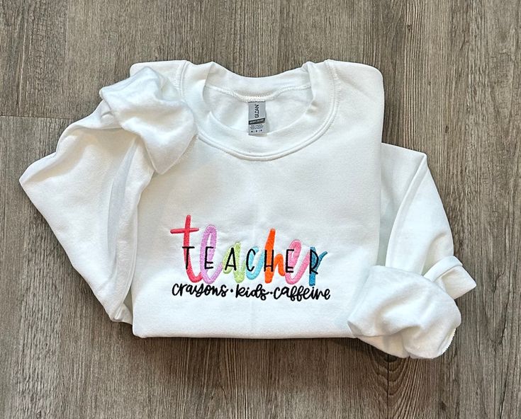 "Colorful Embroidered TEACHER Sweatshirt, Teacher Sweatshirt, Teacher Appreciation Gift for Teacher Valentine Gift, School Teacher Shirt HOW TO ORDER:  1) From the first dropdown menu, select sweatshirt size 2) From the second dropdown menu, select sweatshirt color 3) Click \"Add to Cart\" SIZING & SWEATSHIRT INFO: - Embroidery design is 5x7, the design will appear smaller on larger shirts - Larger Fit. If between sizes, we recommend sizing down - Sweatshirts are 18000 Gildan® Heavy Blend™ Adult Crewneck Sweatshirts IMPORTANT ORDERING INFORMATION: - Please review the sizing charts, with measurements, that are in the listing photos before purchasing.  CANCELLATIONS: - Cancellations are accepted within 24 hours of placing your order. After that, your order is possibly in production and we ca School Spirit Tops With Letter Embroidery, Casual Tops With Embroidered Text For School, Long Sleeve Tops With Multicolor Embroidery And Letter Print, Multicolor Embroidered Long Sleeve Top With Letter Print, Multicolor Embroidery Long Sleeve Top With Letter Print, Long Sleeve T-shirt With Multicolor Embroidery, White School Spirit Tops With Letter Embroidery, White Tops With Letter Embroidery For School Spirit, Long Sleeve School Tops With Embroidered Text