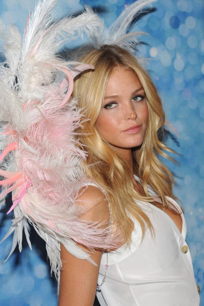 a woman with blonde hair wearing a pink and white feathered headpiece in front of a blue background