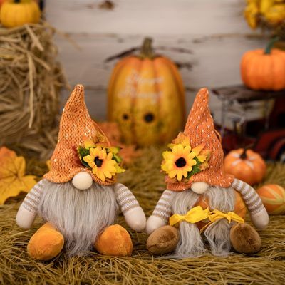 two gnomes sitting in hay with sunflowers on their heads and pumpkins behind them