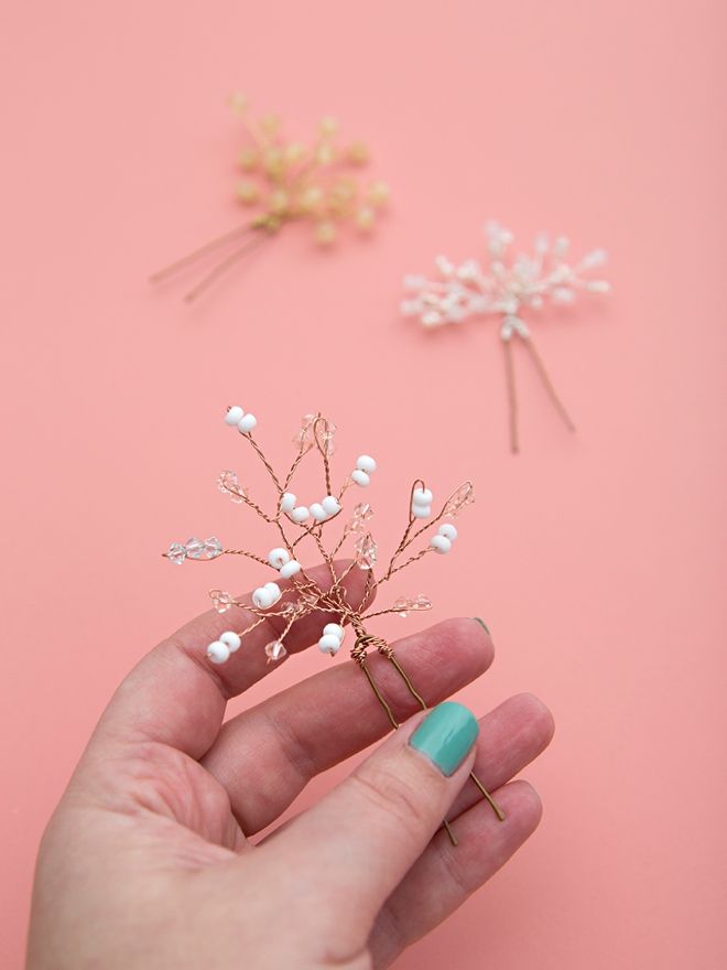 a hand holding a small white flower on top of a pink surface next to two pins