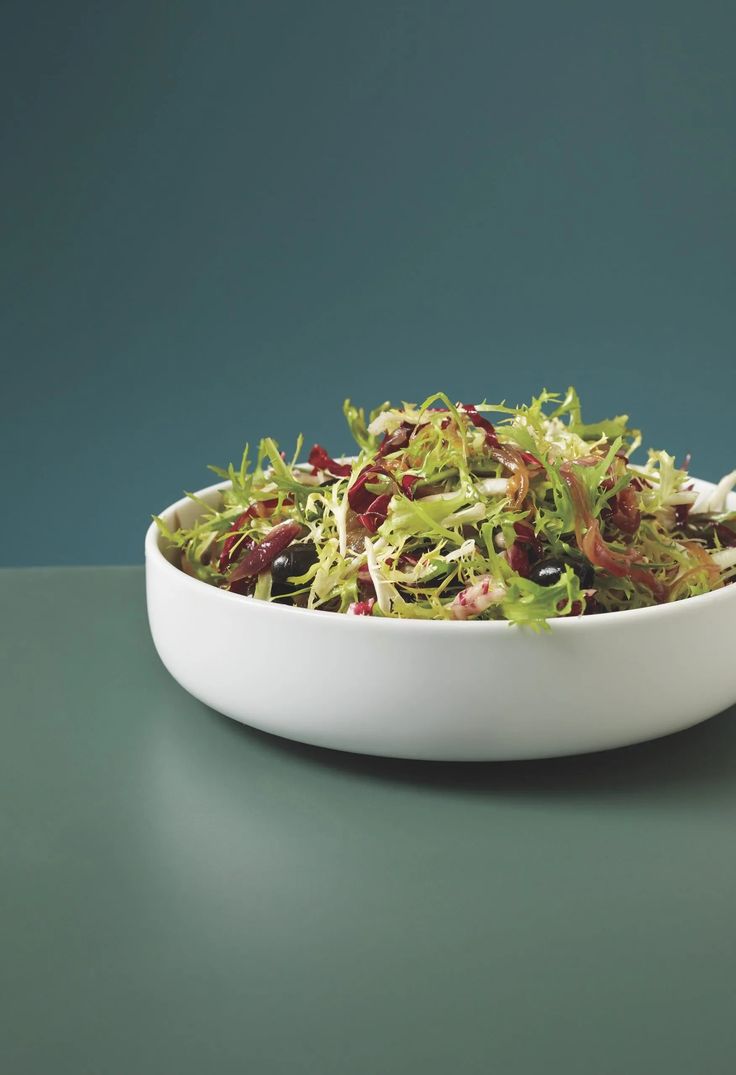 a white bowl filled with salad on top of a green countertop next to a fork