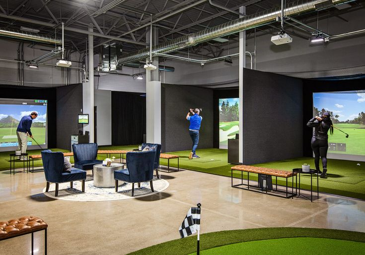 people playing golf in an indoor facility with large screens on the wall and green grass