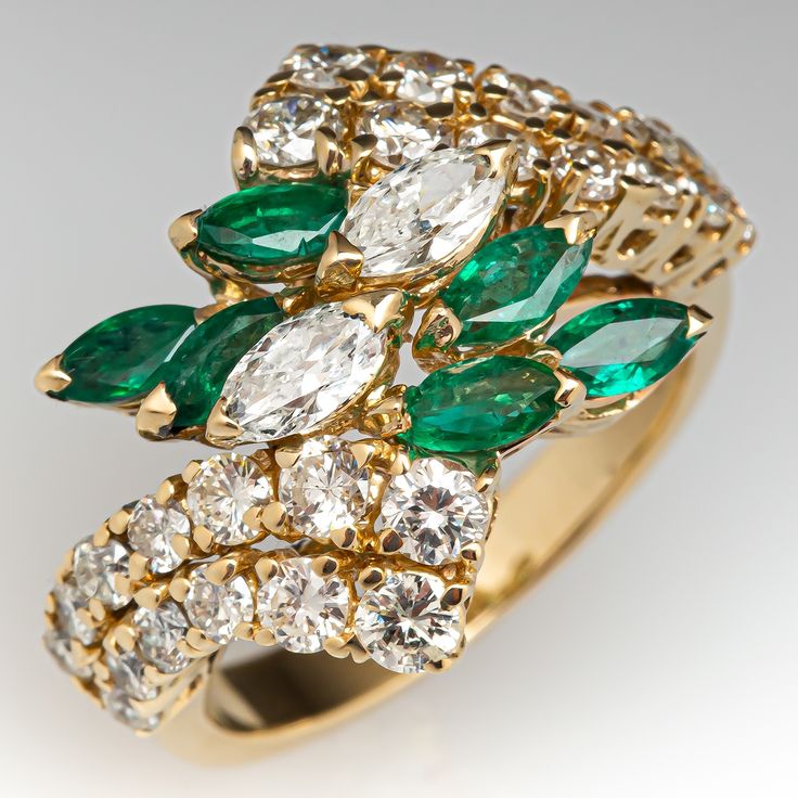 This pretty ring is centered with a cluster of two (2), prong set, marquise brilliant cut diamonds and six (6), prong set, marquise mixed cut natural emeralds. The top face of the by-pass style shank is accented with twenty-six (26), prong set, round brilliant cut diamonds. The ring measures 18.0mm at the top, rises 8.0mm above the finger, tapering to 2.9mm wide and 1.1mm thick at the base of the shank. This ring is currently a size 7. Luxury Marquise Emerald Ring With Prong Setting, Marquise Emerald Diamond Ring With Brilliant Cut, Marquise Brilliant Cut Emerald Ring, Marquise Emerald Ring With Brilliant Cut, Fine Jewelry Emerald Ring With Marquise Brilliant Cut, Fine Jewelry Marquise Emerald Ring With Brilliant Cut, Fine Jewelry Diamond Emerald Ring Marquise Cut, Fine Jewelry Marquise Cut Diamond Emerald Ring, Emerald Marquise Jewelry With Brilliant Cut