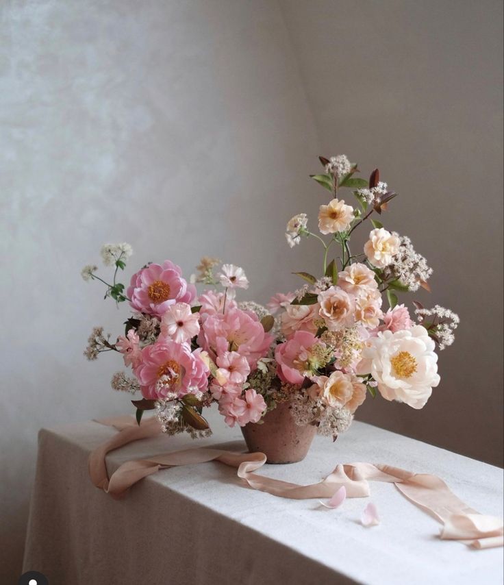 a vase filled with pink and white flowers sitting on top of a table next to a ribbon