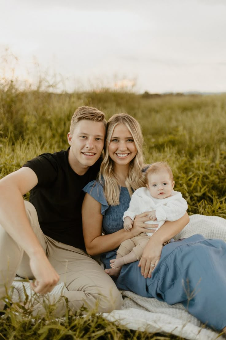 a man and woman holding a baby on a blanket in the middle of a field