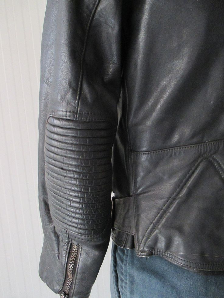 "Super 70s black biker jacket. Genuine leather. Made in Germany. It's a very solid jacket, with reinforced shouders and elbows (pic. 4-7), such as the bottom on backside (pic.8). Front black plastic zipper and mandarin collar that closes with velcro (pic.2). There are two front zipped pockets (pic.3) whose lining has to be repaired as it is unsewn. There are two other zipped pockets on waisband (pic.4-5). Two buckled straps on waistband. Quilted lining with inner pocket (pic.10). Very good condi Fall Cafe Racer Biker Jacket For Motorcycling, Fitted Moto Biker Jacket, Retro Leather Jacket With Zipper For Biker Events, Retro Biker Jacket With Zipper For Biker Events, Fitted Moto Biker Jacket For Motorcycling, Fitted Biker Leather Jacket, Fitted Biker Leather Jacket For Urban Adventures, Fitted Moto Leather Jacket For Motorcycling, Moto Leather Jacket With Zip Fly For Motorcycling