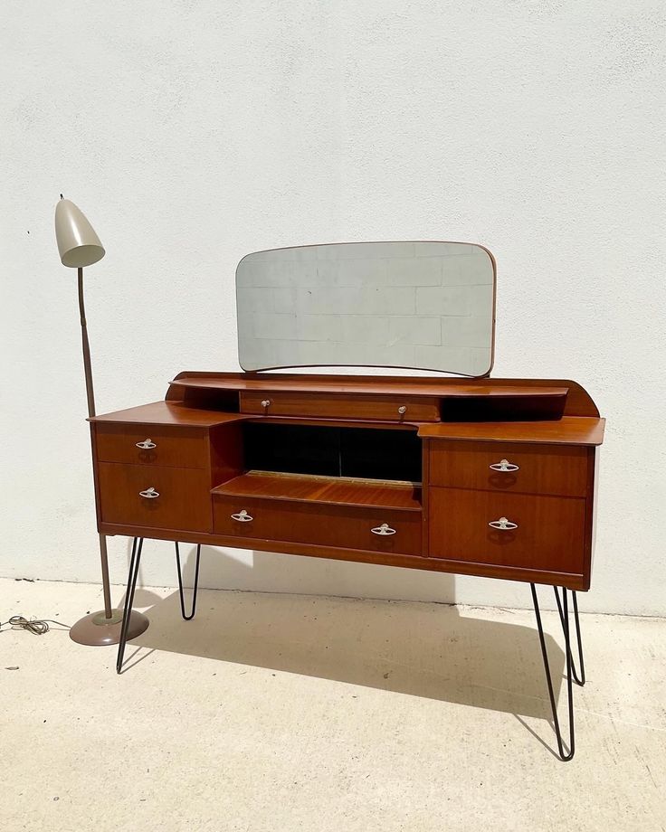 a wooden desk with a mirror on top and hair dryer next to it in front of a white wall