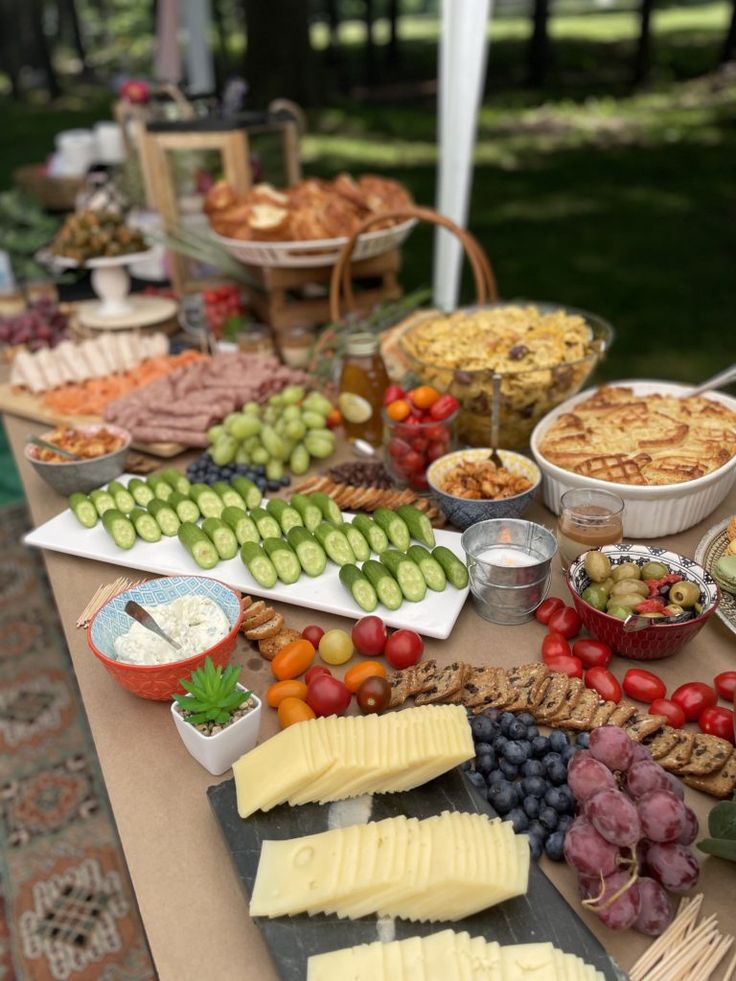 an assortment of cheeses, fruits and crackers on a table outdoors with other snacks