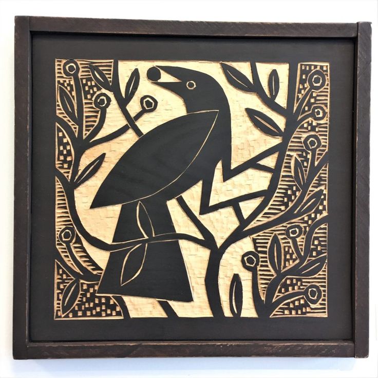 a black bird sitting on top of a tree branch next to leaves and berries in a wooden frame