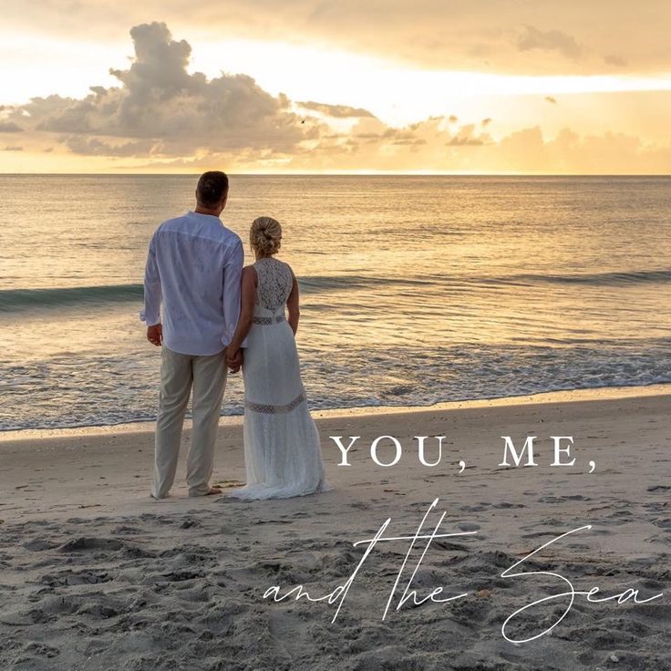 a man and woman standing on top of a beach next to the ocean at sunset