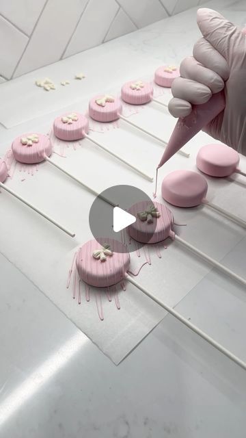 a person in white gloves is decorating pink desserts with icing and sprinkles