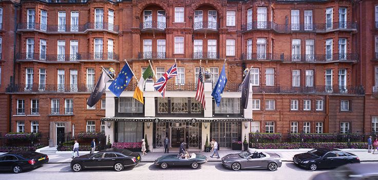 cars parked in front of a hotel with flags on the building's windows and balconies