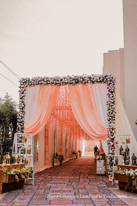 an outdoor ceremony with white drapes and pink flowers on the aisle, surrounded by greenery