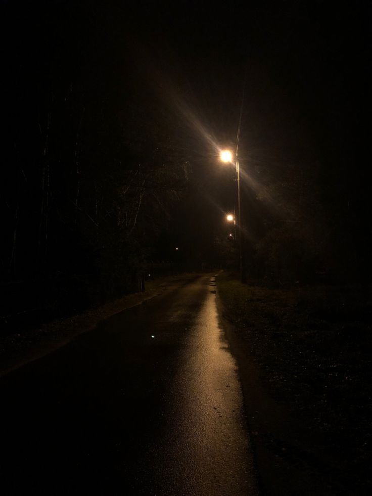 an empty road at night with street lights shining on the side and trees in the background