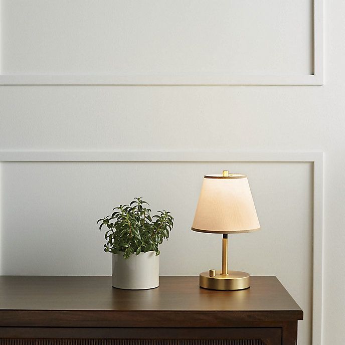 a table with a lamp and a potted plant on it next to a white wall