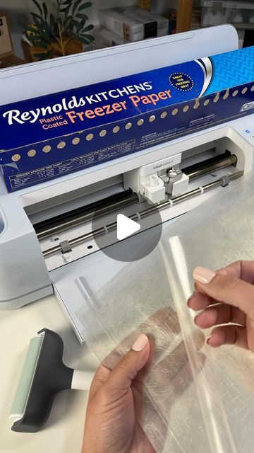 a person is using a machine to cut paper on a piece of clear plastic with scissors