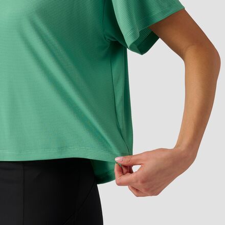 a woman in a green shirt and black pants with her hands on her hip, looking down