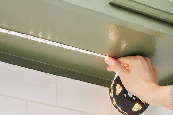 a hand is holding a light strip above the ceiling