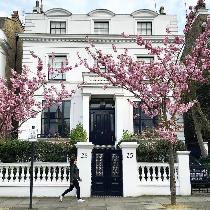 a woman walking down the sidewalk in front of a building with pink flowers on it