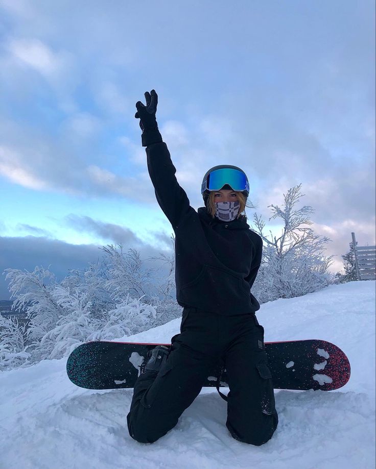 a person sitting in the snow on top of a snowboard with their arms up