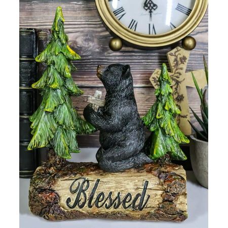 a bear statue sitting on top of a wooden log next to a clock and evergreen trees