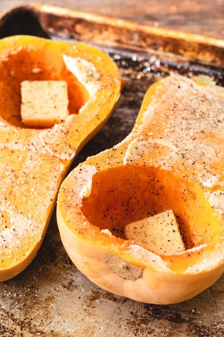 two buttered squash halves sitting on top of a baking pan covered in seasoning