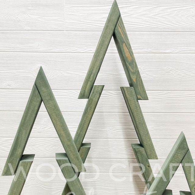 three wooden christmas trees are on display against a white wood wall, one is green and the other is brown