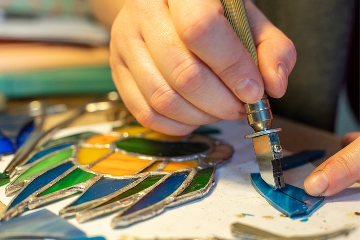 a person is working on stained glass with a small metal object in front of them