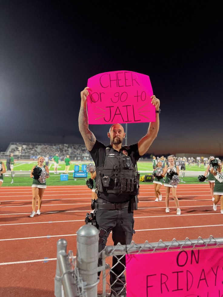 a man holding up a pink sign in front of a crowd on a track at night