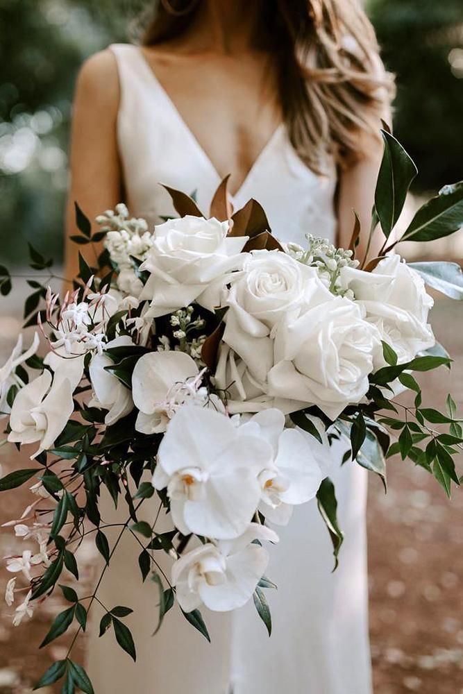 a woman in a white dress holding a bouquet of flowers and greenery on her wedding day