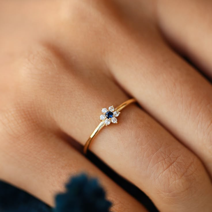 a woman's hand wearing a gold ring with blue and white flowers on it