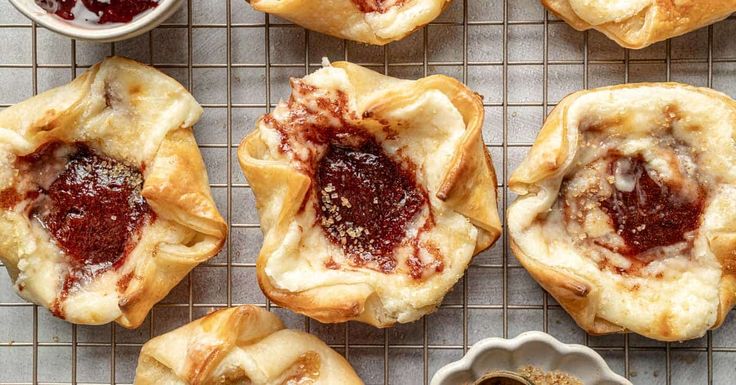 several pastries on a cooling rack with jam in the middle and small bowls next to them