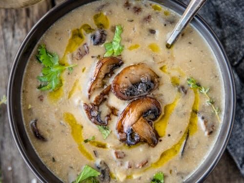 a bowl filled with soup and mushrooms on top of a wooden table next to a spoon