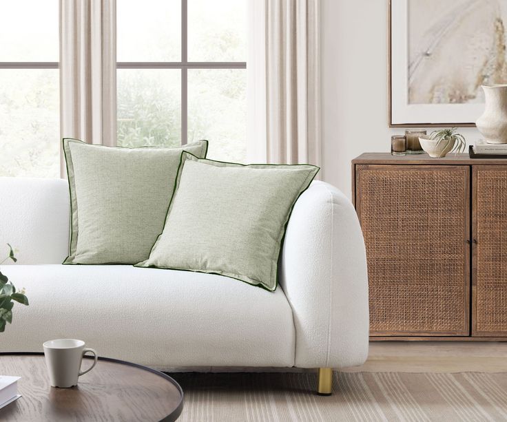 a living room with white couches and green pillows