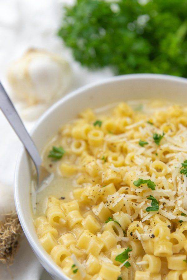 a white bowl filled with macaroni and cheese on top of a table next to garlic