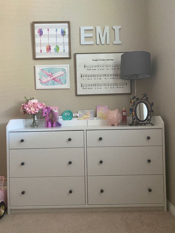 a white dresser with drawers and pictures on the wall