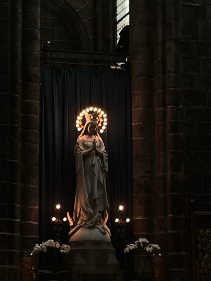 the statue is surrounded by candles in front of a black curtained wall and windows